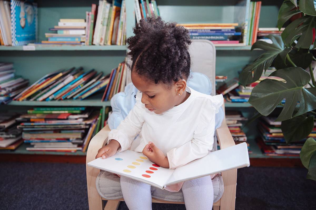 Preschool girl sitting in a chair reading a book